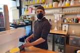 man frothing milk with mask on at cafe