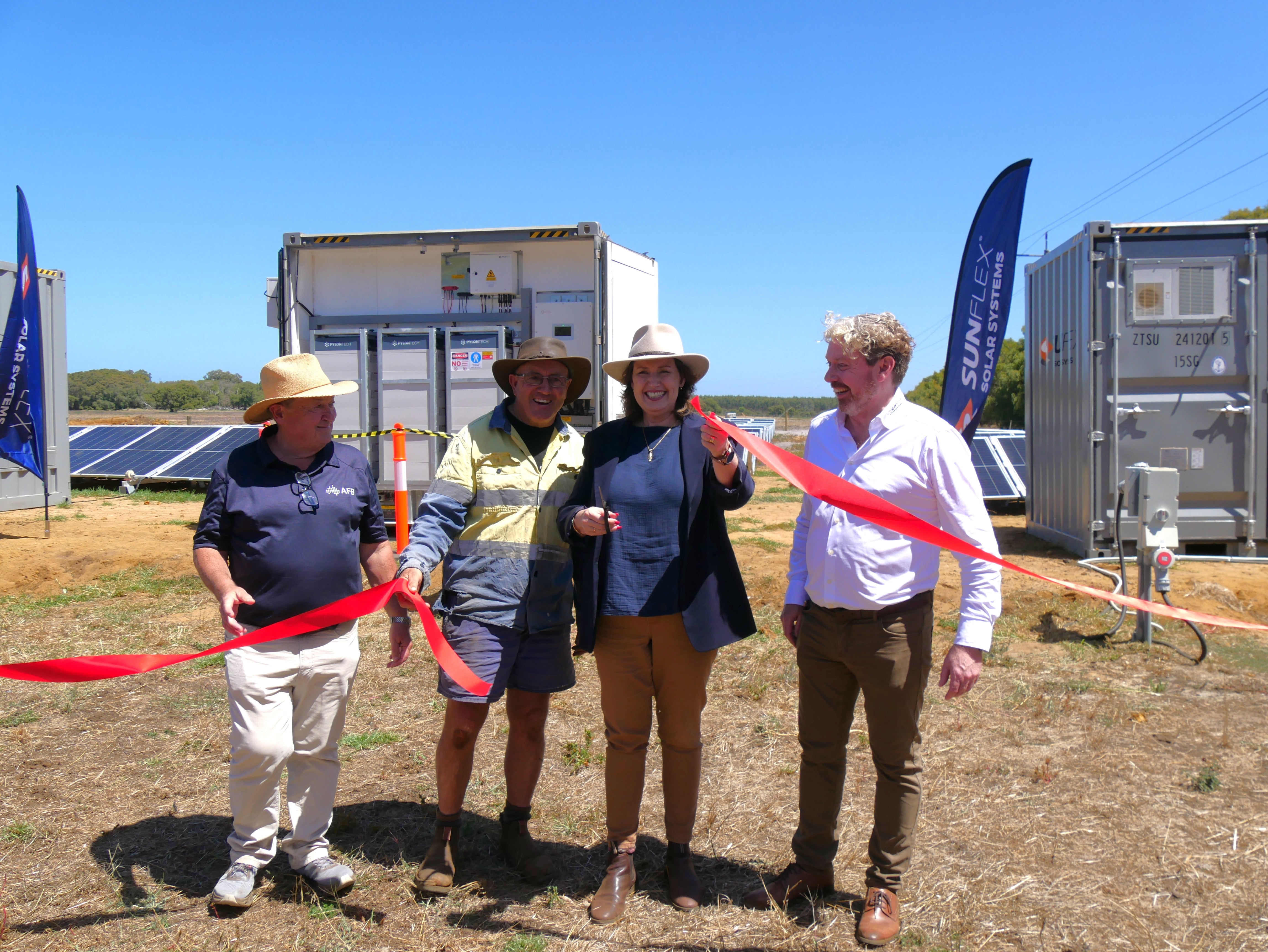 Four people standing behind red cut ribbon smile at camera.