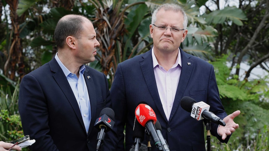 Two men in suits in front of trees at press conference