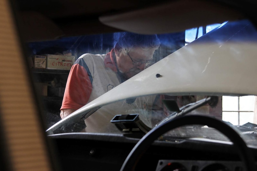 Peet Menzies looking into the lifted bonnet of a vintage car.