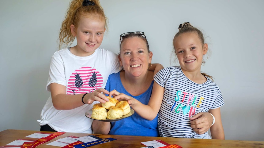 Woman and two young daughters stand holding scones.