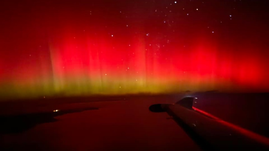 Red and yellow lights glowing above land with a plane wing in view