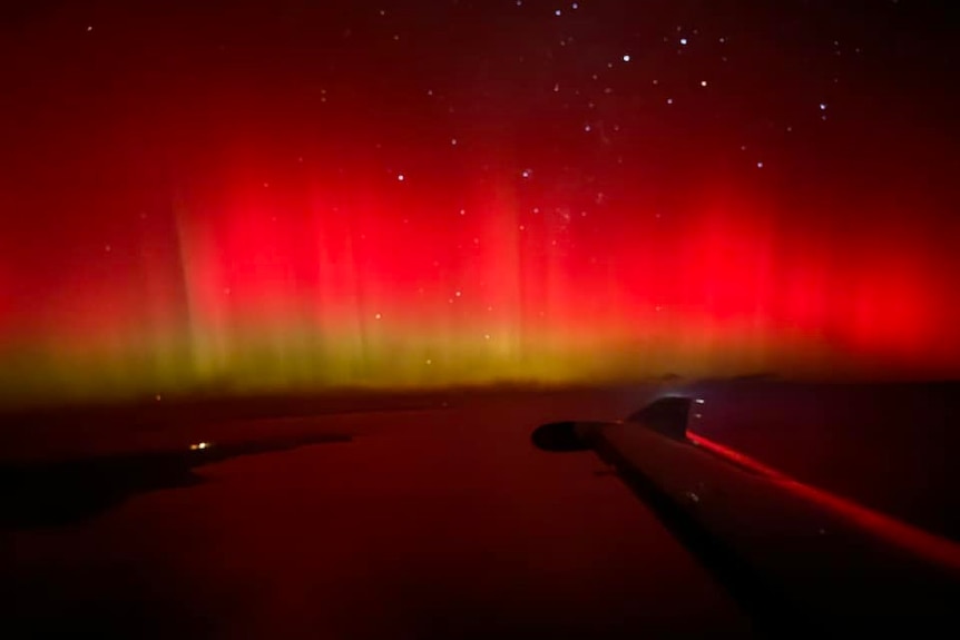 Red and yellow lights glowing above land with a plane wing in view
