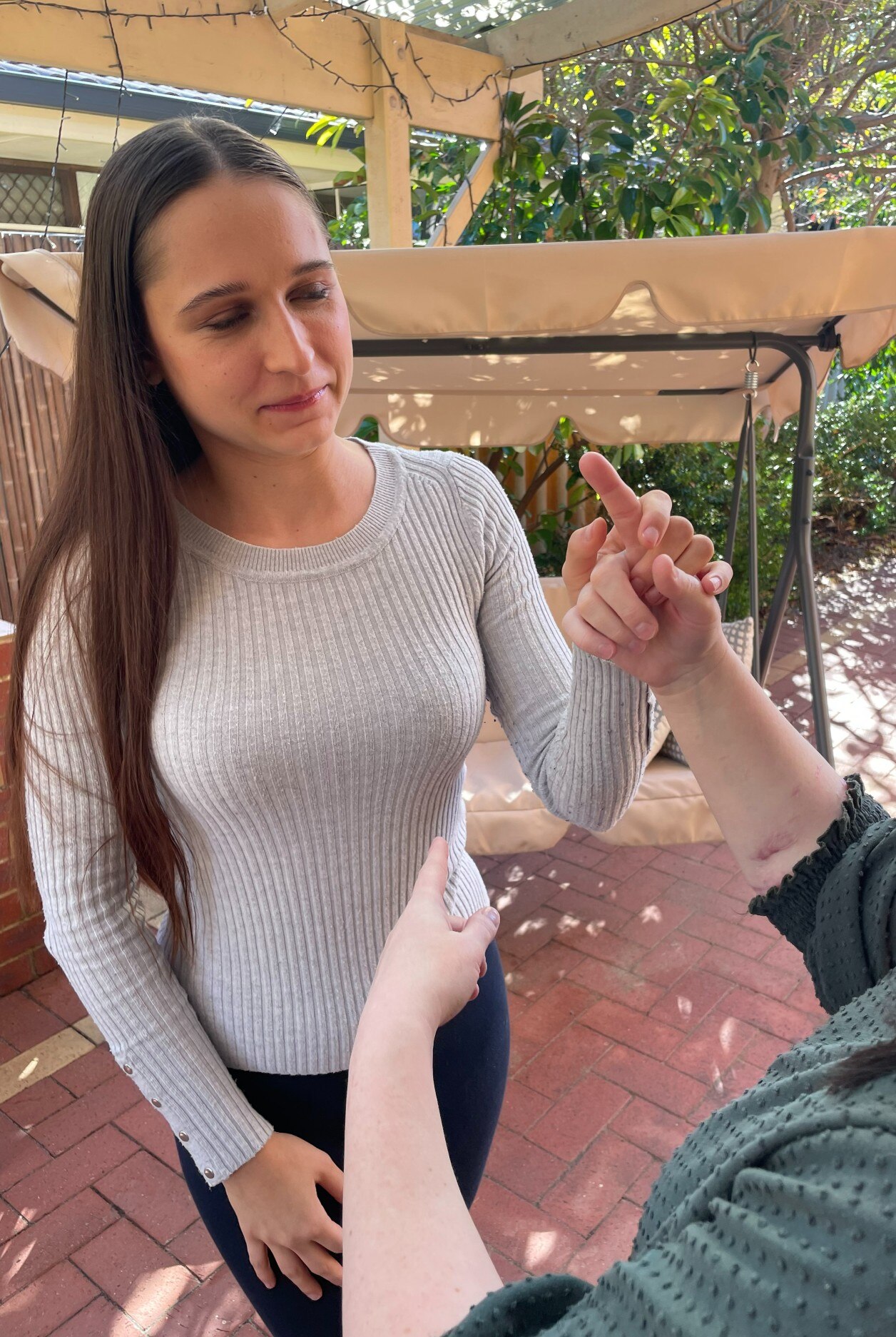 Vanessa in the backyard with her hand feeling over the hand of another woman, whos is pointing her index finger.