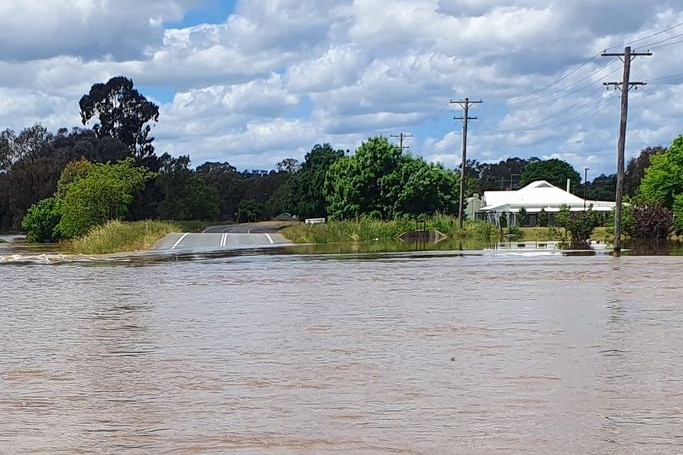 Flood water over a road with a house and trees in the background