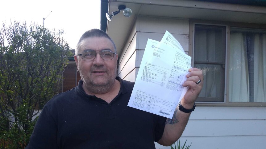Man holds electricity bill in his hand outside his Molong home.