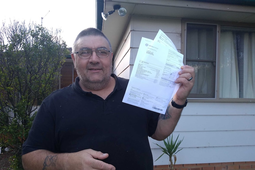 Man holds electricity bill in his hand outside his Molong home.