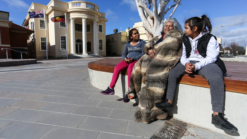 Esther Kirby sitting in the main street of Kerang with two young Indigenous girls, Aneeka and Jayla.