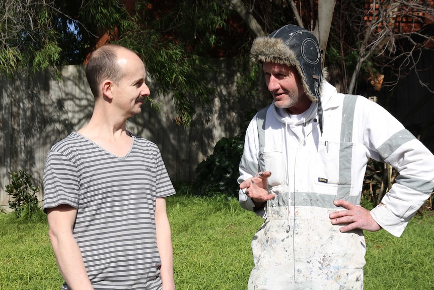 Two men, one strangely dressed, stand talking to each other.