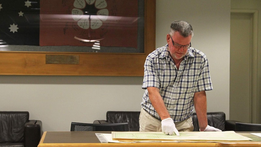 NT Library's Brian Hubber stands in the library looking over a vintage map of Humpty Doo.
