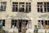 Ukrainian soldiers stand in front of a building with a Ukrainian flag on it