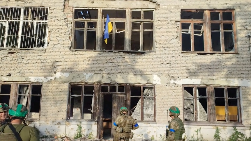 Ukrainian soldiers stand in front of a building with a Ukrainian flag on it