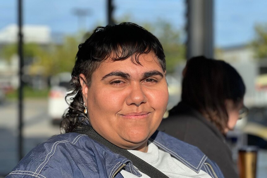 Young indigenous woman with short hair smiling, wears denim jacket.