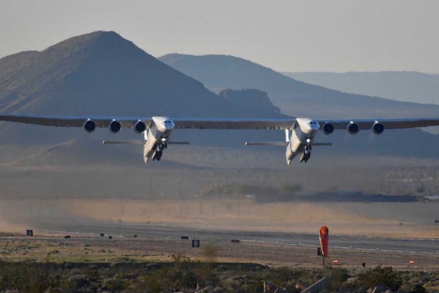 The stratolaunch jet leaves the ground from an airstrip in the desert.