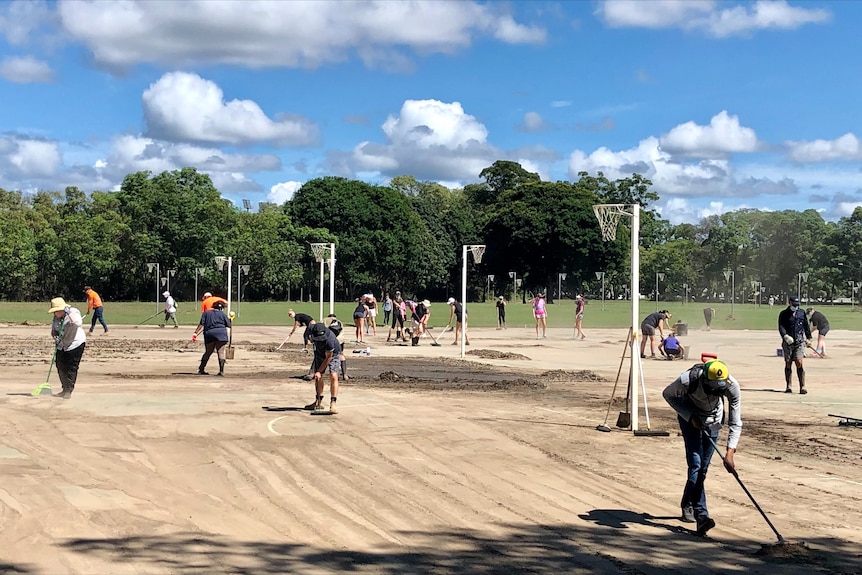 Workers scrub a muddy netball court.