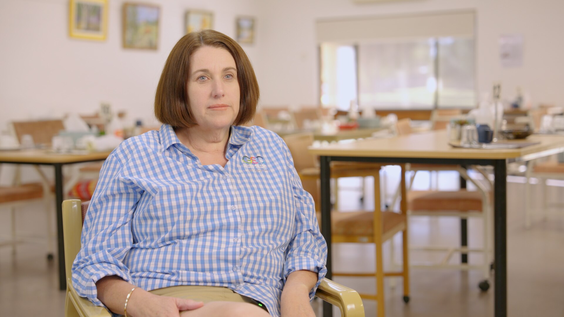 Woman sits in chair inside aged care facility dining room