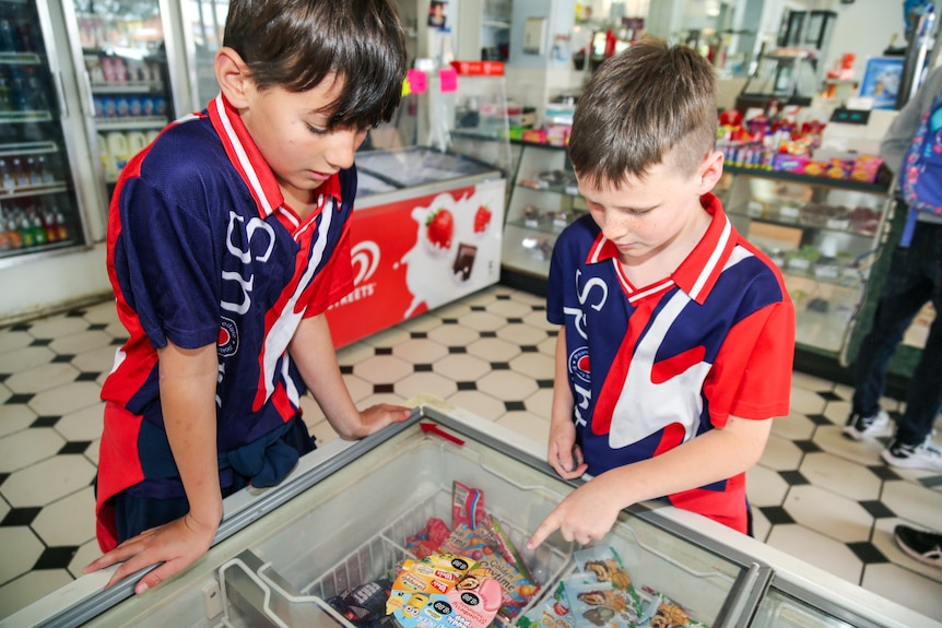 Two boys look at an ice cream fridge trying to decide what to choose