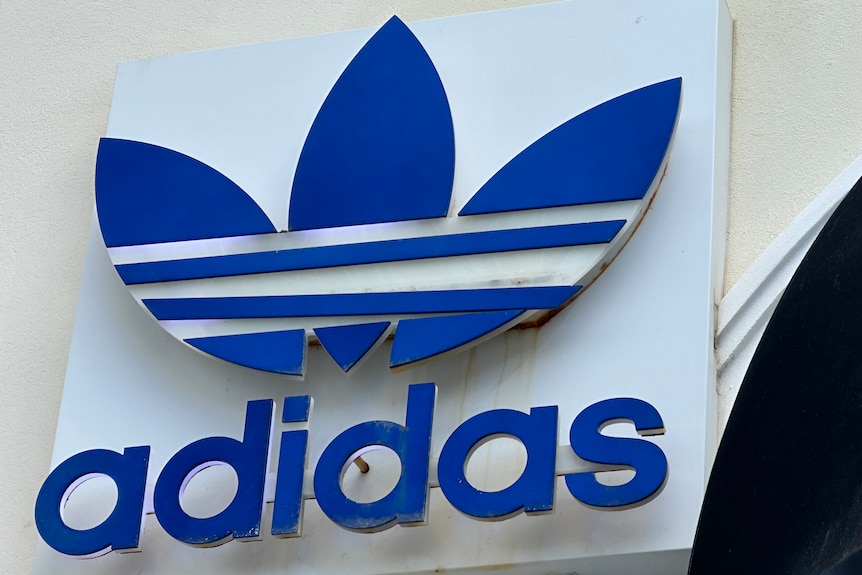 Blue sign featuring the adidas logo affixed to a building exterior.