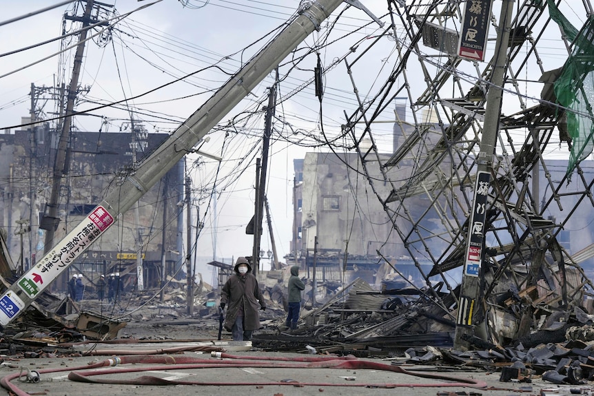 A view of a street with powerlines fallen down. A person walks wearing a face mask.