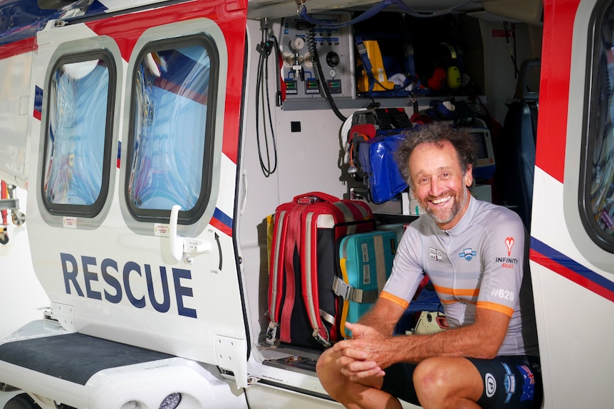A smiling man sits in the back of a grounded rescue helicopter 