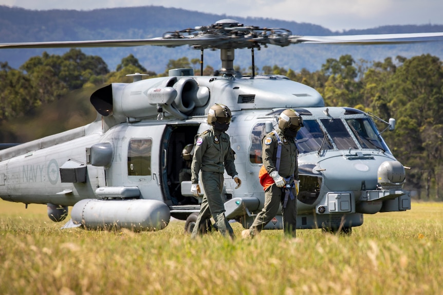 People in military gear walk away from a grounded helicopter.