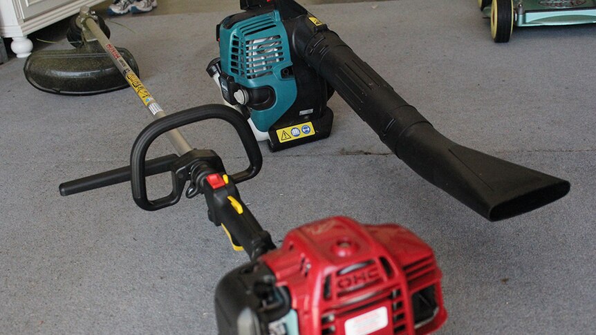 A weed cutter and leaf blower sitting on the floor of a garage.