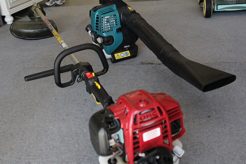 A weed cutter and leaf blower sitting on the floor of a garage.