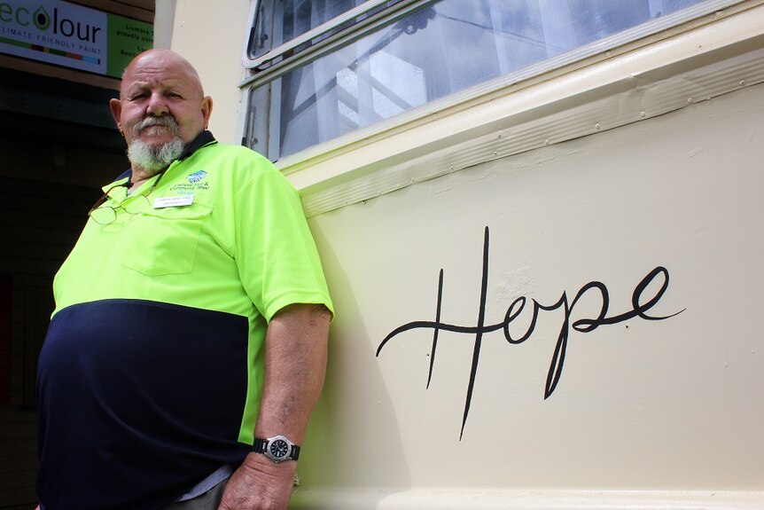 A man in a high-viz shirt stands next to a caravan with the word 'hope'