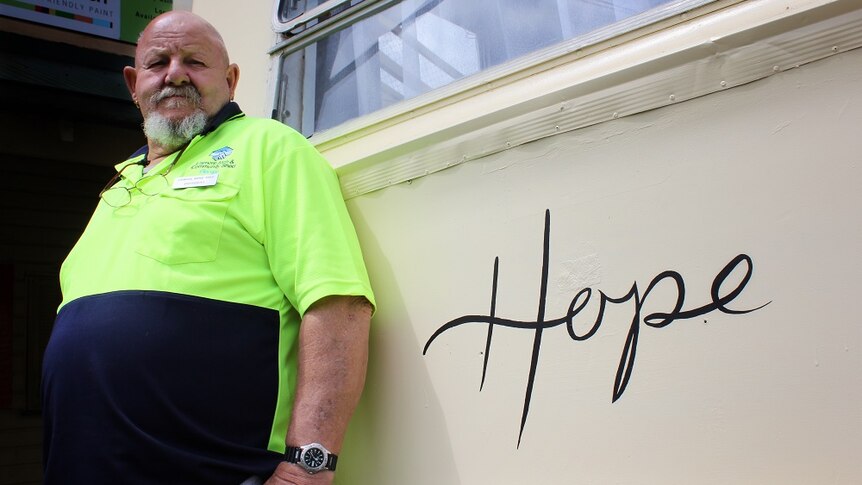 A man in a high-viz shirt stands next to a caravan with the word 'hope'