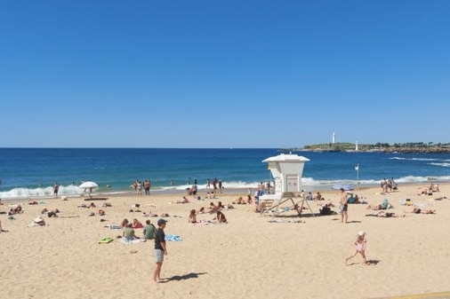 People lie on a beach under blue skies