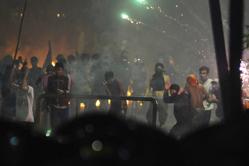 Men throw flares and other objects amid tear gas on a dark Jakarta street.