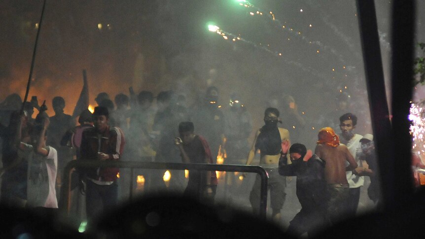 Men throw flares and other objects amid tear gas on a dark Jakarta street.