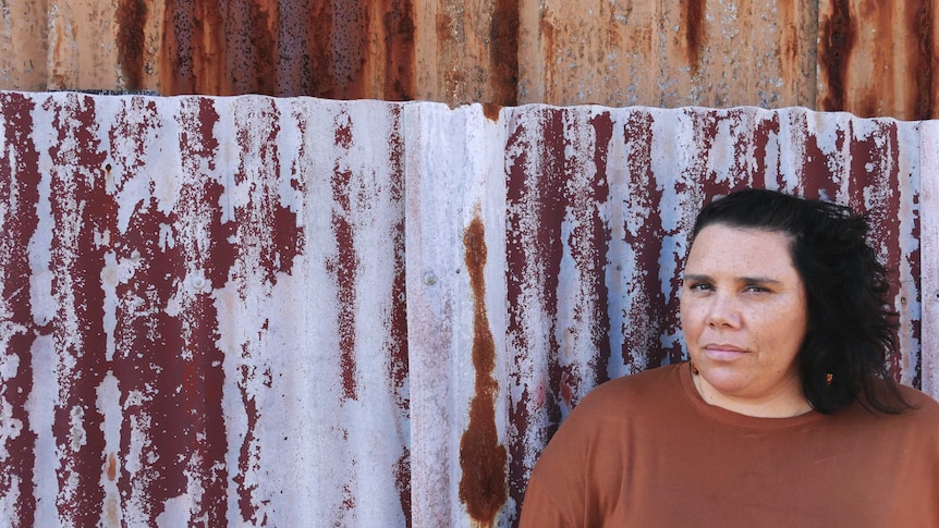 An Aboriginal woman standing in front of a corrugate iron background