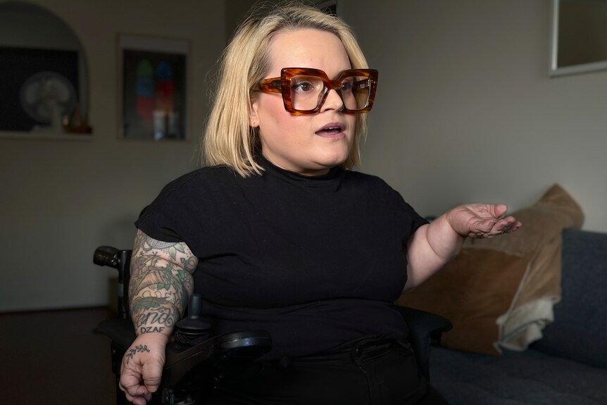A woman in glasses sitting in a power wheelchair.