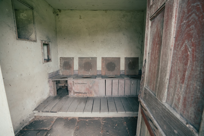 A row of four privy drop toilets inside a building.
