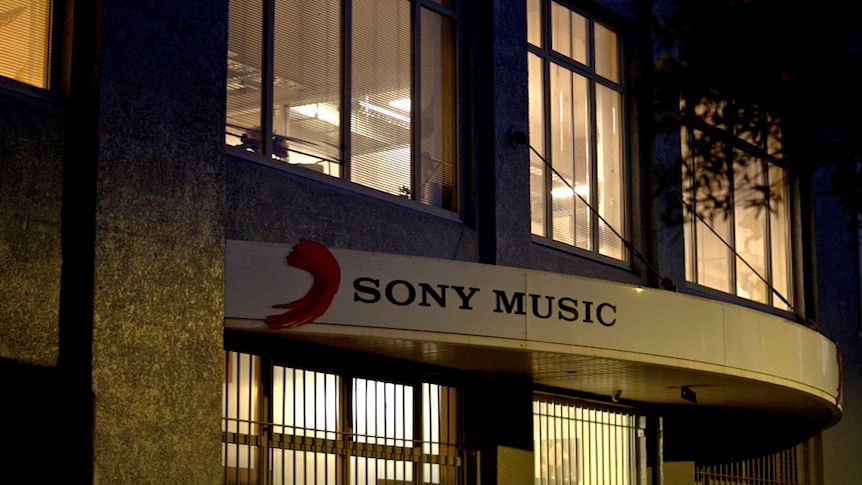 A two-story office building at night, there are lights on inside and a sign above the door says Sony Music.