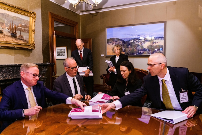Four men and two women in an office with large written reports in front of them