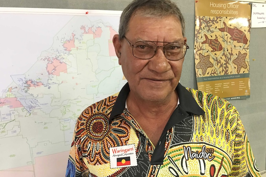 A mid shot of Des Hill standing indoors in front of a map wearing a Waringarri Corporation shirt.