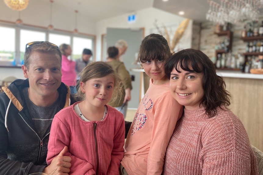 A father, mother and two girls smiling in a restaurant.