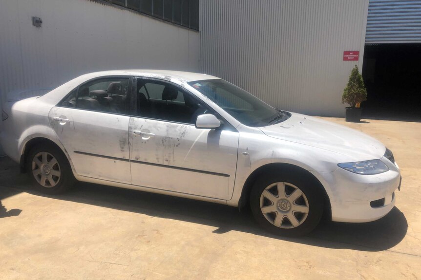 A damaged white sedan parked in front of a warehouse