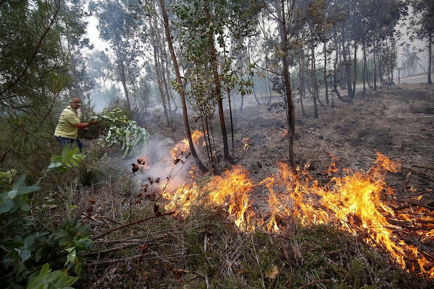 A man uses a branch with leaves to fan out flames