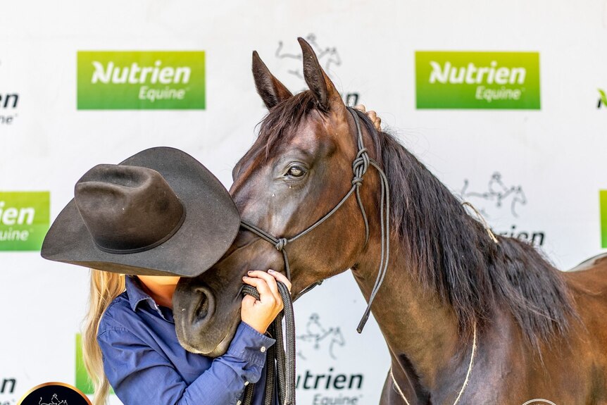 A woman in a black hat kisses a black horse on the nose.
