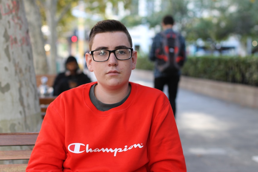 boy with glasses sitting on bench in city street 