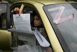 A woman places a ballot paper into a box from her car window.
