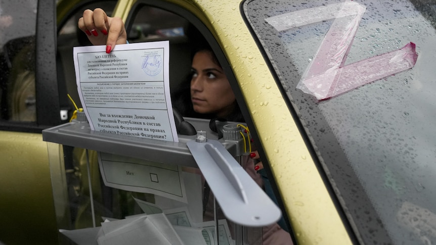 A woman places a ballot paper into a box from her car window.