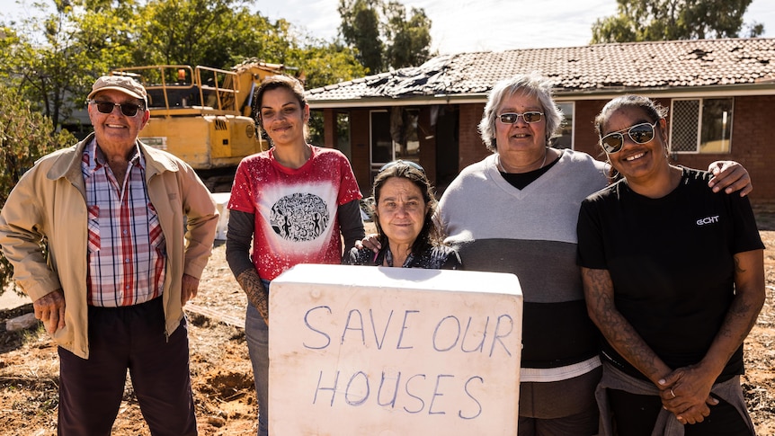 A group of five people holding a sign saying SAVE OUR HOUSES outside a house scheduled for demolition.  