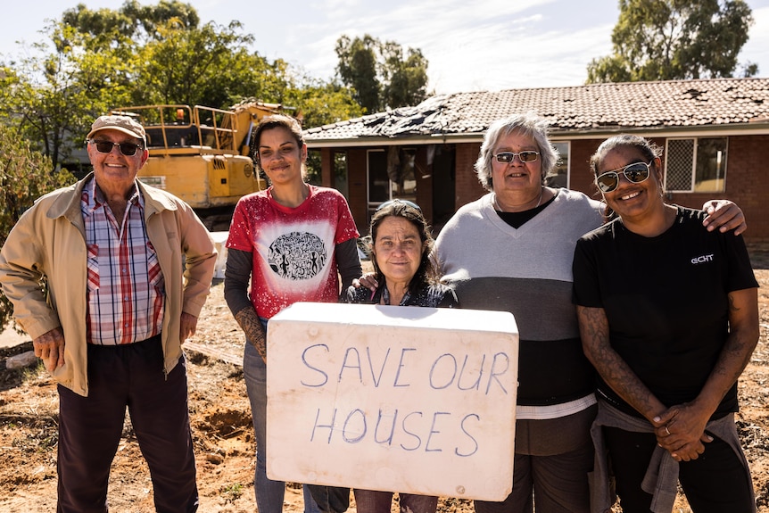 A group of five people holding a sign saying SAVE OUR HOUSES outside a house scheduled for demolition.  
