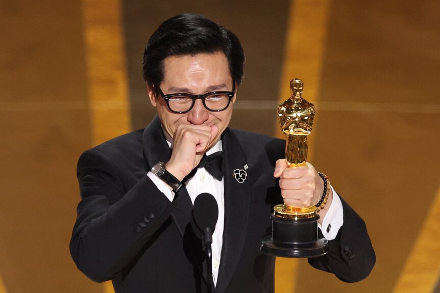Ke Huy Quan holding an Oscar holding back tears