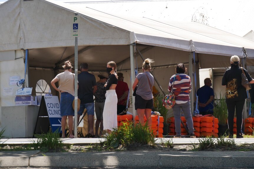 White COVID testing clinic tent with a line of six people out the front all wearing masks.