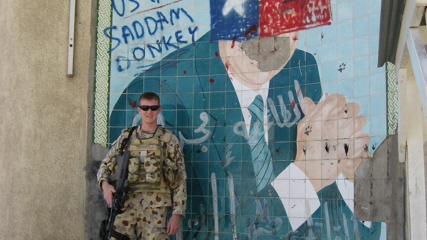 Rodney Hargrave poses with his weapon in front of a Saddam Hussein painting graffiti-ed with the words: 'US GOOD SADDAM DONKEY'